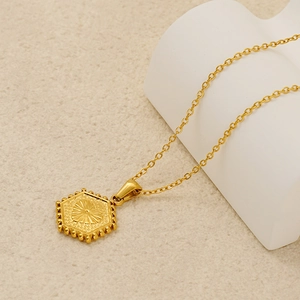 Detail of 18K gold hexagon pendant necklace with radial texture on a white geometric stand