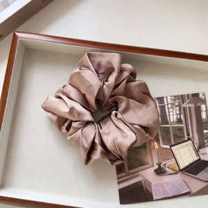 Close-up of champagne satin scrunchie with soft pleats on a wooden display tray