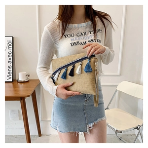 Detail showing beige woven texture fabric clutch with blue and white tassels