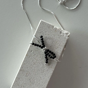 Close-up of black bead bow pendant on a silver snake chain over textured stone base