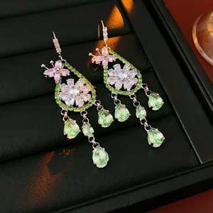 Dettaglio di orecchini d'argento con fiori rosa e nappe in zircone verde in una scatola nera