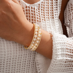 Detailed shot of triple-layer pearl bracelet with gold diamond accents on a model sleeve