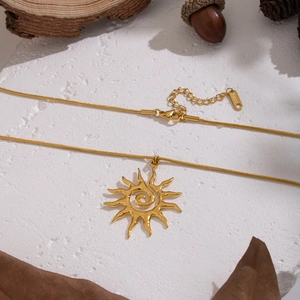 Golden sun pendant necklace with snake chain displayed on natural stone and wood
