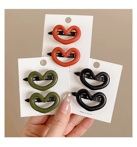 Close-up of sweet heart-shaped hair clips in orange, olive green and black on card