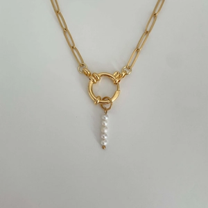 Detail of a gold link chain necklace featuring a central ring and a cluster of white pearls