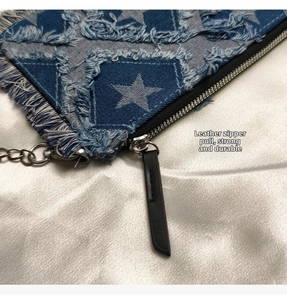 Detail of blue denim bag with star pattern, frayed edges and leather zipper puller