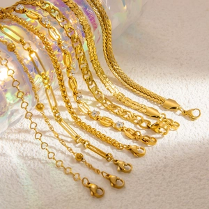 Close-up of assorted 18k gold plated Cuban, heart, and snake chains on a textured surface