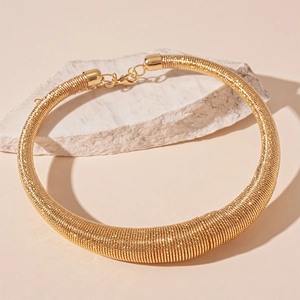 Detailed view of bold golden coiled metal choker necklace on a white stone background
