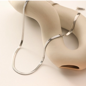 Close-up of a silver flat snake chain necklace draped over a ceramic artistic display