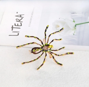 Detailed view of the gold-tone spider brooch with emerald green gemstones and enamel finish
