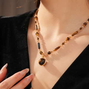 Detailed view of a vintage necklace with brown tiger eye beads and a gold pendant on a model