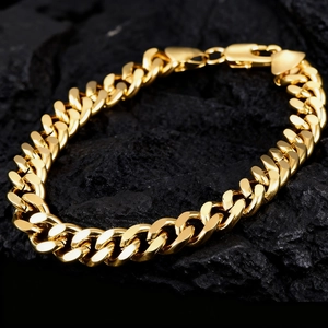 Polished golden stainless steel Cuban link bracelet on dark textured stone background
