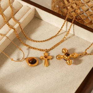 Detailed close-up of golden stainless steel cross pendants on a beige velvet jewelry box