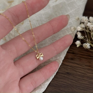 Close-up of golden bow necklace with white pearl detail held over a natural background