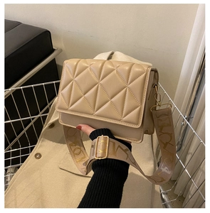Detail of beige quilted crossbody bag with wide patterned strap and gold metal buckle