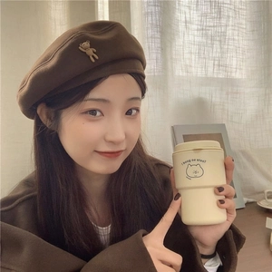 Detail of a brown wool beret featuring a cute 3D bear accessory and a stylish coffee cup