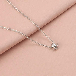 Macro detail of a silver octopus pendant on a fine chain over pink fabric