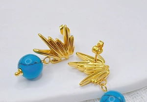 Détail macro de boucles d'oreilles dorées avec design rayon de soleil et perles turquoise