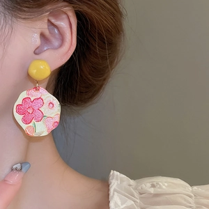 Macro shot of woman wearing floral sunflower earrings with yellow studs and pink petals