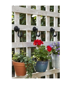 Retro black cast iron wall hooks shown holding hanging plants on white wooden fence