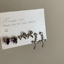 Macro detail of three-piece Gothic earring set featuring purple heart and silver bow