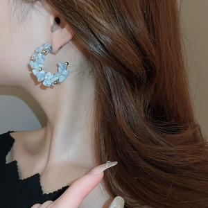 Minimalist C-shaped hoop earrings with blue gravel and gold beads worn by a model