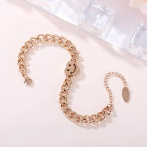 Bracelet chaîne en acier rose doré avec pendentif cœur sourire sur fond rose doux