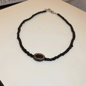 Close-up of black beaded necklace with a gold-bordered oval pendant and star detail
