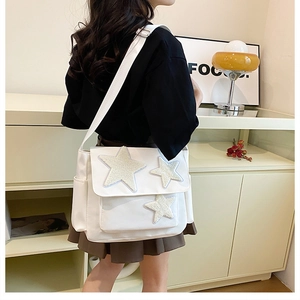 Side view of white canvas messenger bag with star patches showing size and fit