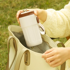 Close-up of white coffee mug with leather strap being placed in a beige leather bag