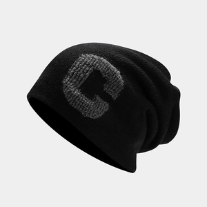 Close-up of the grey knitted letter C on the side of a black ribbed beanie hat