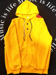 Détail du sweat à capuche jaune avec texture gaufre, poche kangourou et boutons noirs