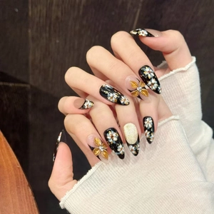 Detail of handmade stiletto nails featuring 3D gold flowers and black cat eye finish