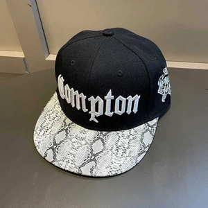 Detail of Compton embroidery on black snapback hat with white snakeskin textured brim