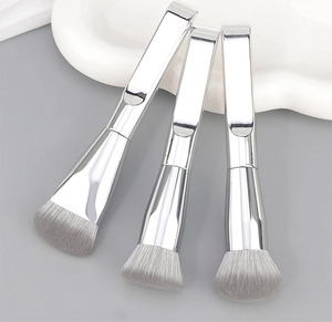 Set di tre pennelli da trucco argentati con setole grigie dense su un vassoio elegante