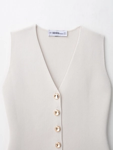 Detailed close-up of beige knit vest featuring a deep V-neck and gold metal buttons