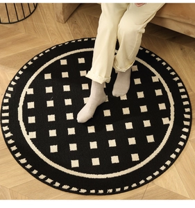 Detail of round black and white checkered carpet on wood floor with cozy sofa background