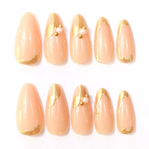 Detail of long almond press-on nails with nude pink base, gold foil, and pearl accents