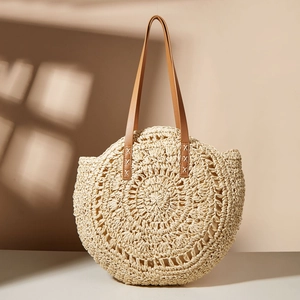 Detail of woven straw tote bag with intricate floral patterns and brown leather straps