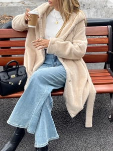 Photo street style d'une femme en manteau peluche beige et jean évasé sur un banc en bois