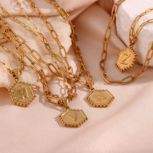 Double-layered paperclip chain necklace with gold hexagonal letter pendants on silk background