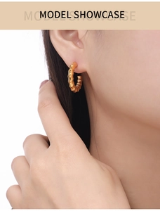 Macro view of gold-plated bamboo texture C-shaped hoop earrings worn by a model