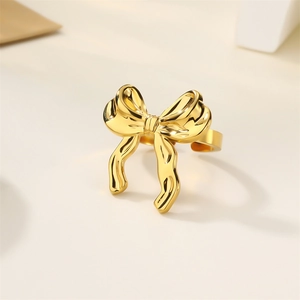 Macro shot of 18k gold butterfly bow ring with pearl detail on a beige background