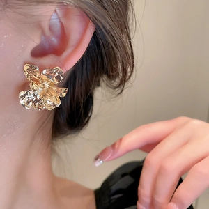 Close-up of a model wearing a gold metallic flower earring with irregular petal design
