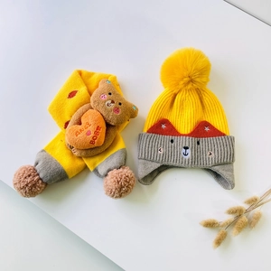 Detail of yellow knit hat and scarf set with cute plush bear and heart decoration