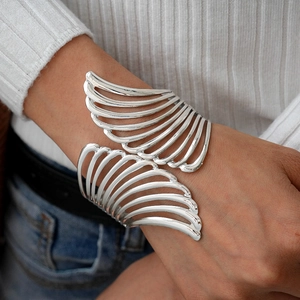 Detail of silver hollow wing cuff bracelet worn by a model against a casual background