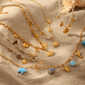 Gold ocean necklaces with shell star and turtle pendants on beach sand background