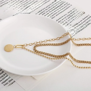 Dettaglio della collana dorata a strati con pendente rotondo inciso Good Luck