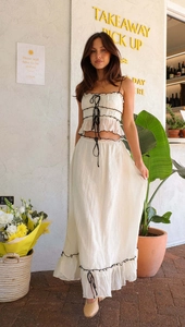 Detail of white two-piece set featuring pleated crop top with black lace-up bow and long skirt