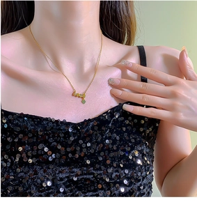 Detail of gold love necklace with green heart pendant on a model wearing black dress